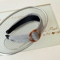 Detalle de diadema de tela gris con adorno de resina ámbar sobre rejilla metálica - Gris