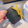 Detail view of mustard yellow velvet bow hair clips on two green metal U-shaped bases - Yellow