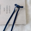 Detail einer dunkelblauen Samtschleife-Haarspange mit langen Bändern auf einem Buch - Blau