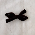 Detail of elegant dark brown velvet bow hair clip on a textured fabric background - Brown