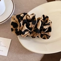 Close-up of leopard print satin hair scrunchie accessory on white ceramic tray - Smudged Color