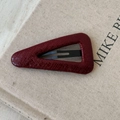 Detail of dark red faux leather hair clip with crocodile texture on a beige background - Red Large Triangle Style