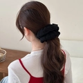 Large black knit scrunchie with brand tag on ponytail in cozy home interior setting - Black