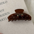 Detailansicht der dunkelbraunen Kirsch-Haarklammer mit roten Strasssteinen auf Buch - Braune Haarkralle