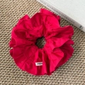 Detail shot of a red ruffled hair scrunchie with FMdre label on woven texture - Red