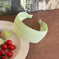 Close-up of light green pleated fabric headband on a wooden table with rustic background - Green
