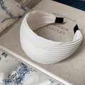 Detalle de diadema de tela plisada crema sobre un libro antiguo con luz suave - Blanco