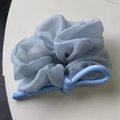 Dettaglio di scrunchie in organza azzurro con fiocco di seta e trama arricciata - Blu