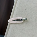 Macro view of light pink marble texture acetate hair clip with gold logo detail - Pink