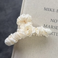 Elegante pinza para el cabello de satén plisado crema sobre un libro decorativo - Blanco