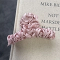 Detalle de la tela de satén plisada rosa que envuelve la pinza de metal sobre un libro - Rosa