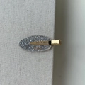 Detailed view of silver glitter oval hair clip with gold metal base on fabric - Silver