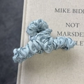 Primer plano de una pinza para el cabello de satén plisado azul claro en un libro - Azul