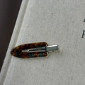 Close-up of tortoise shell acetate hair clip with gold logo on beige book surface - Blue Brown Gradient