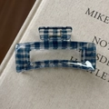 Dettaglio della pinza per capelli a quadretti blu con molla dorata su un libro - Stile Rettangolare