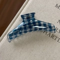 Dettaglio di una molletta per capelli a scacchi blu e bianchi su un libro materico - Gruccia Stile