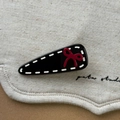 Vue détaillée d'une pince noire en goutte d'eau avec nœud rouge sur toile beige - Noir