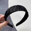 Close-up of black pleated fabric headband with matte silk texture and flexible inner frame - Black