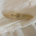 Gros plan d'une barrette vintage en acétate avec strass floraux sur tissu blanc brodé - Blanc Sirène
