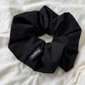 Detail of a black pleated scrunchie with Oulifang logo tag on a white fabric background - Black
