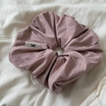 Dettaglio scrunchie in raso rosa con etichetta logo a fiocco su sfondo di tessuto morbido - Rosa