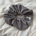 Detail view of a grey scrunchie with twill texture and a small bow logo tag - Gray