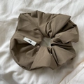 Detailed close-up of a khaki fabric scrunchie with a minimalist bow logo label on white linen - Brown