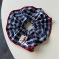 Detail eines dunkelblauen Karo-Scrunchies mit roten Nähten und Bären-Illustrations-Tag - Kariertes Haargummi