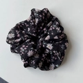 Detail van chiffon haarelastiekje met roze madeliefjespatroon op zwarte stof - Zwart