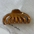 Detailed macro view of large amber wood grain acetate hair claw clip on beige fabric texture - Brown
