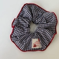 Detailansicht von marineblauem Karo-Haargummi mit roter Kante und Textiletikett - Karo-Haargummi
