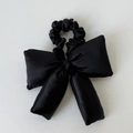 Détail d'un grand chouchou nœud bouffant en satin noir avec un lustre doux et des coutures denses - Noir
