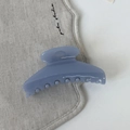 Gros plan d'une pince à cheveux mate bleu brume en acrylique au design incurvé sur lin - Bleu clair