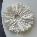 Detailed macro view of white pleated fabric scrunchie with pearl bow accents - Off-white