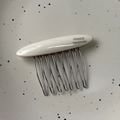 Detailed macro view of acetate hair comb featuring ten wavy metal teeth and gold label - Milk White