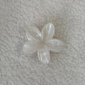 Close-up van de witte plumeria haarklem op een zachte getextureerde stoffen achtergrond - Crèmewit Frangipani