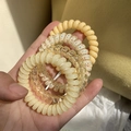 Set di 4 elastici a spirale per capelli color pastello tenuti in mano su sfondo caldo - Serie Gialla