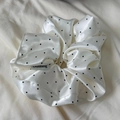 Close-up of a white satin polka dot scrunchie featuring a minimalist logo cloth tag - Scrunchie / White