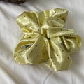 Polka dot yellow satin scrunchie with subtle brand logo on textured fabric background - Yellow
