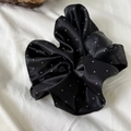 Detail shot of a black satin scrunchie with white polka dots on soft fabric background - Black