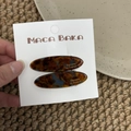 Close-up of tortoise shell acetate hair clips set on a display card in a rustic setting - Blue Brown Gradient