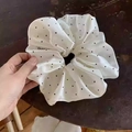 Macro detail of oversized satin scrunchie with classic black polka dots on white fabric - White