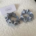Detail of two light blue satin scrunchies with white piping and bead accents on soft rug - Blue