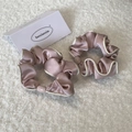 Detailed view of two pink satin hair scrunchies with white piping on a soft plush background - Pink