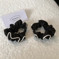 Close-up of black satin hair scrunchies with white piping on a soft plush background - Black