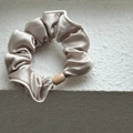 Detail of champagne satin scrunchie with soft sheen and oval decorative buckle - Beige