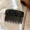 Close-up of a black hair comb with colorful rhinestones on a white fabric background - Black