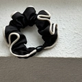 Detailed close-up of a French style black satin scrunchie with cream white piping edge - Black
