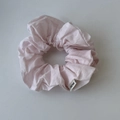 Detail view of pink fabric scrunchie with soft ruffled texture and woven brand label - Pink