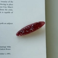 Close-up of translucent burgundy hair clip with glitter sequins on a white book page - Red